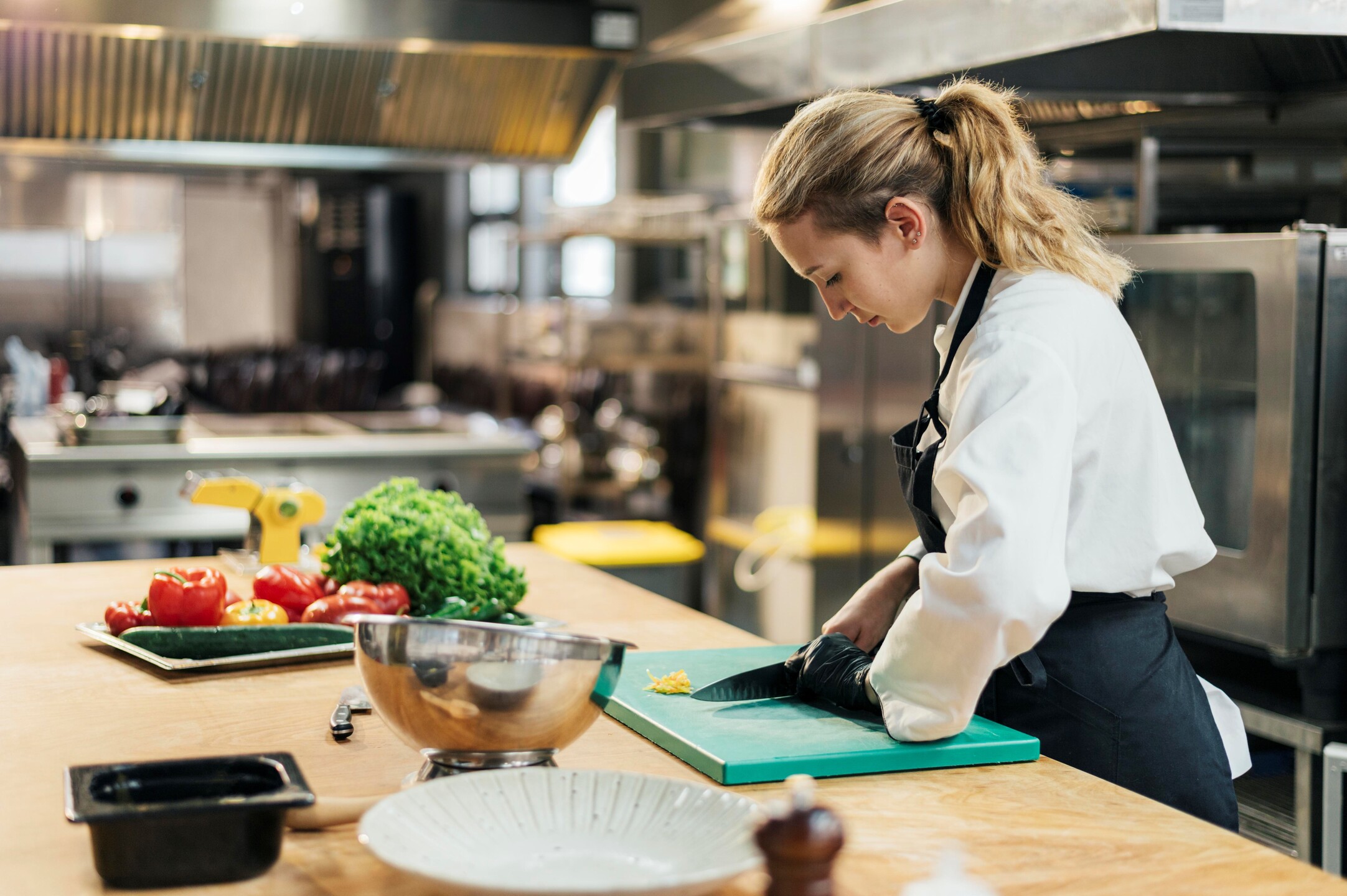 Side-view-female-chef-with-glove-slicing-vegetables-kitchen(1)